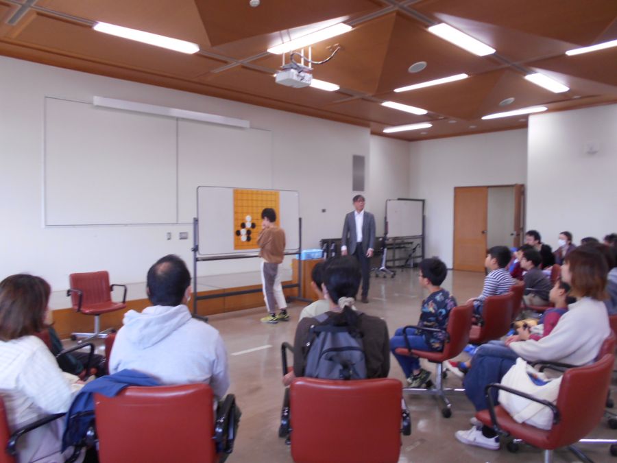 囲碁体験イベントで、参加者の1人が前に出てきて石を打とうとしている写真