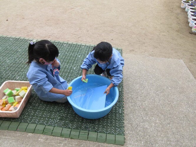 たらいにためた水で粘土板を洗う子どもの写真