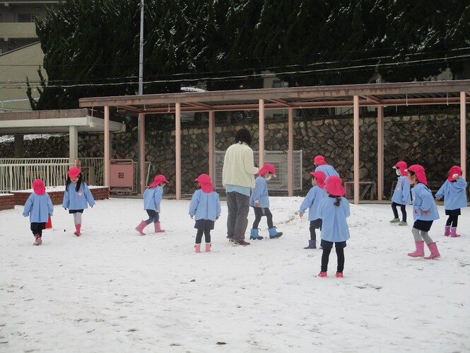 雪の積もった園庭で遊ぶ子ども達の写真