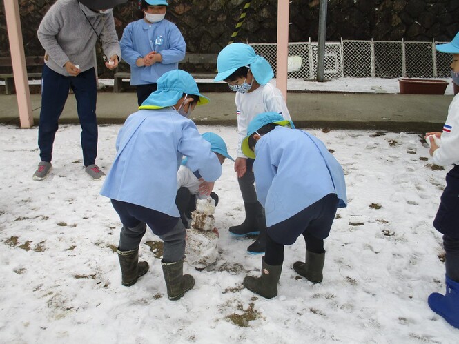 友達と雪だるまを作っている子どもの写真