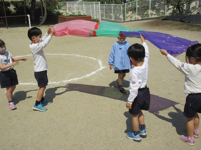 カラーポリ袋の色が地面に反射しているのをみている子どもの写真