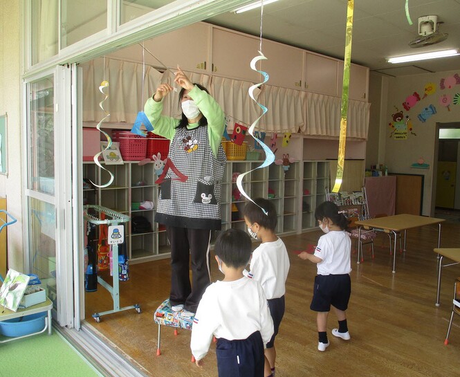 保育室入り口に、先生が飾りをつけている様子をみている子どもの写真