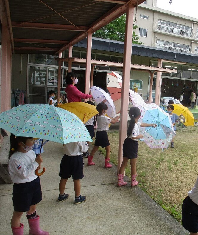 先生や友達と、せーので傘を開いて遊んでいる子どもたちの写真