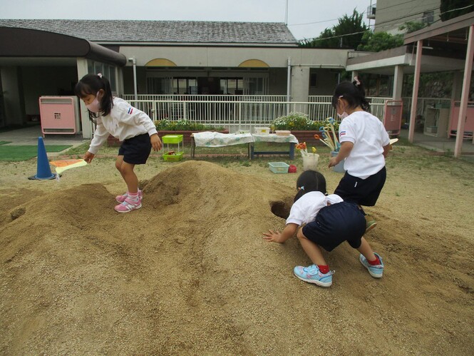 自分の作ったカタツムリのペープサートを、土山にできたトンネルに入れようとしている子どもの写真