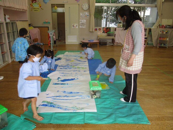 水色の絵の具をローラーで大きな紙に塗っている子どもの写真