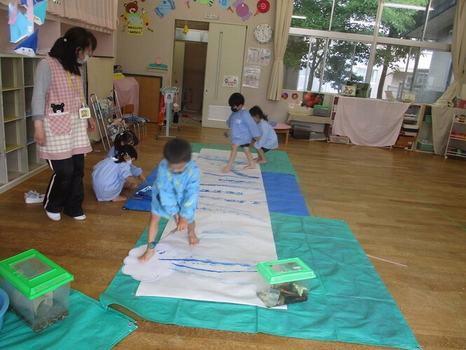 青や水色の絵の具を、ローラーを使って大きな紙に塗っている子どもの写真