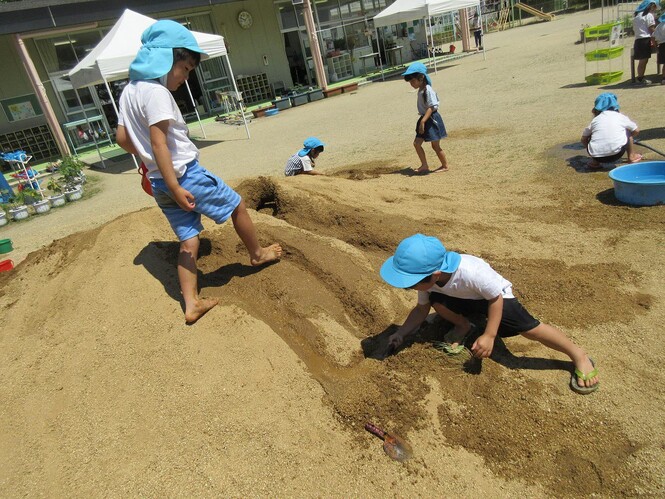 土山に掘った川を、スコップでさらに深く掘っている子どもの写真