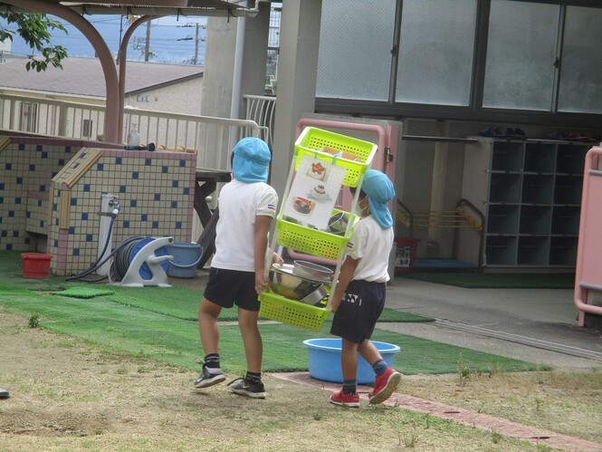 色水遊びに使う道具が入ったワゴンを運ぶ子どもの写真