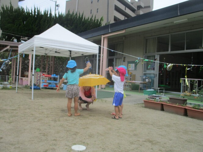 水遊びで、先生のさしている傘に水をかけている子どもの写真