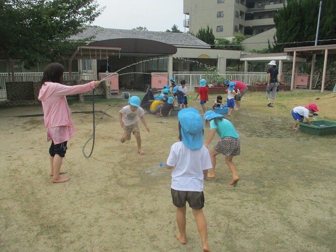 先生がホースの水で作ったトンネルを、水が当たらないようにくぐろうとしている子どもの写真