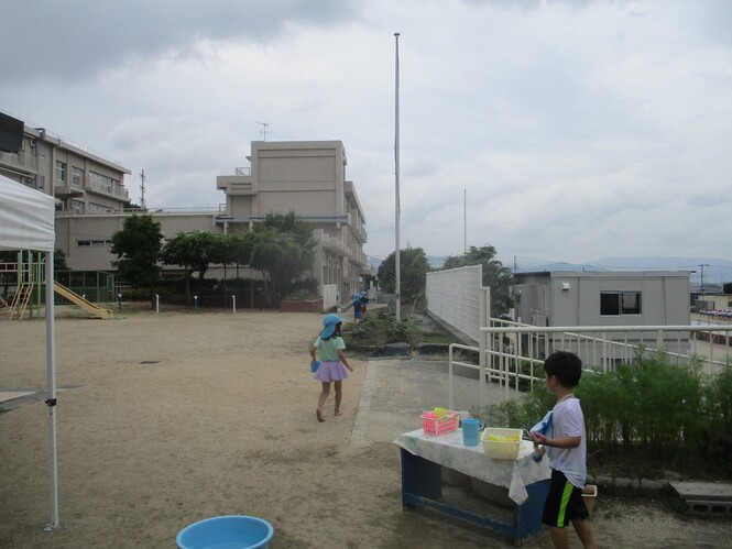 水遊びで残った水を、花壇の花や畑のサツマイモに水をやっている子どもの写真