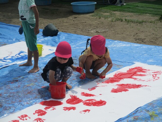 ペインティングタイムで、赤い絵の具を手につけて、紙に塗って楽しんでいる子どもの写真