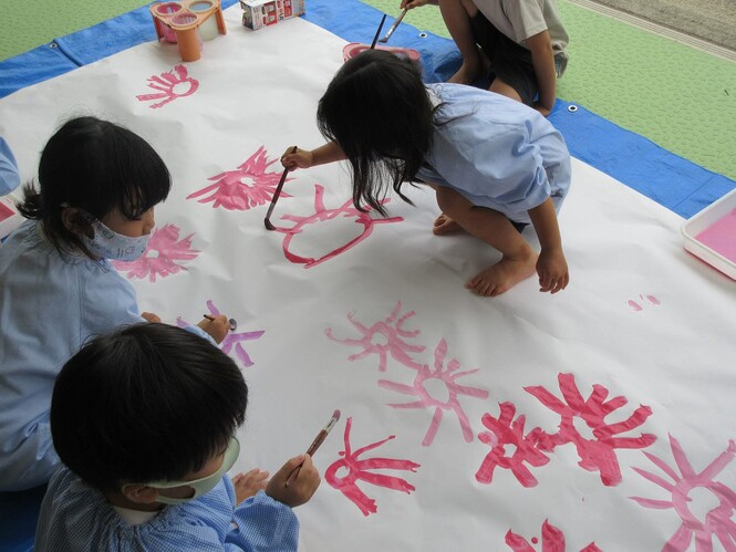 模造紙に絵の具でコスモスの花を描いているもも組子どもの写真