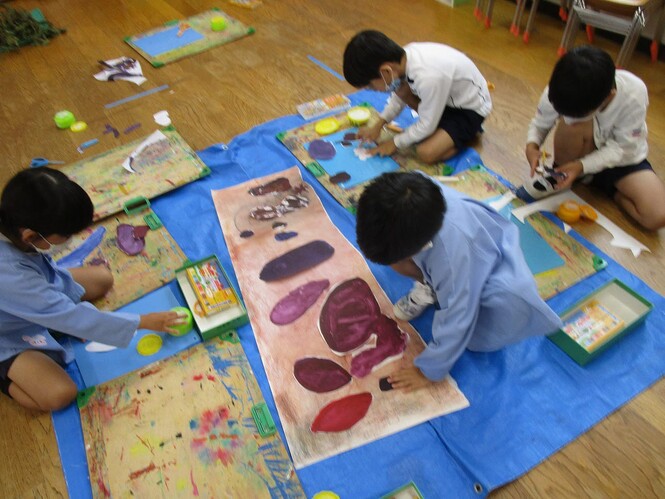 自分の作った芋を切って、コンテで土を描いた画用紙に貼っている子どもの写真