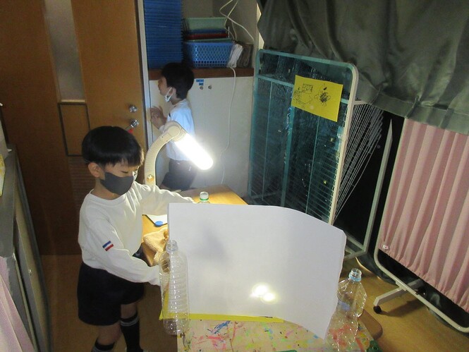 スタンドの光や懐中電灯をあてて影を作ろうとしている子どもの写真
