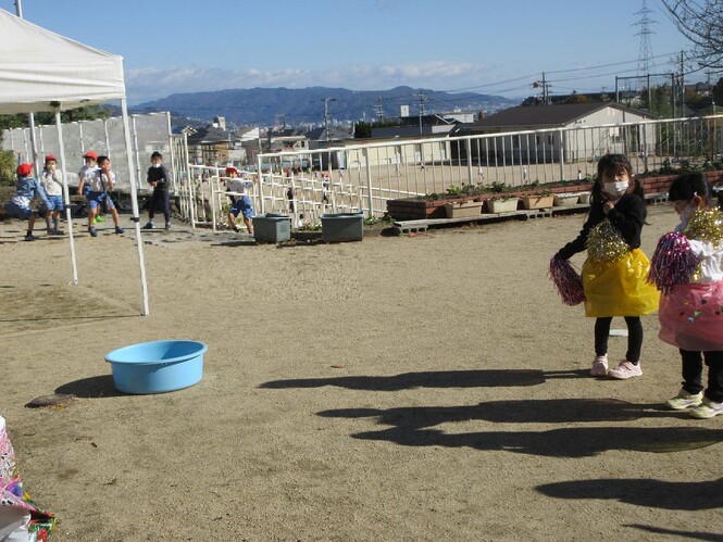 ダンスで遊ぶ園児を離れた場所からみて一緒に踊る小学生の写真