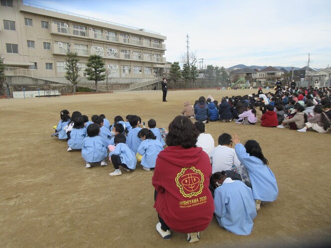 小学校の児童と一緒に、校長先生の話を聞く子どもの写真