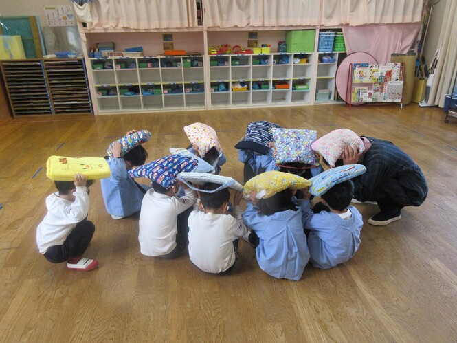 地震避難訓練で、頭を座布団で守ってじっとしている子どもたちの写真