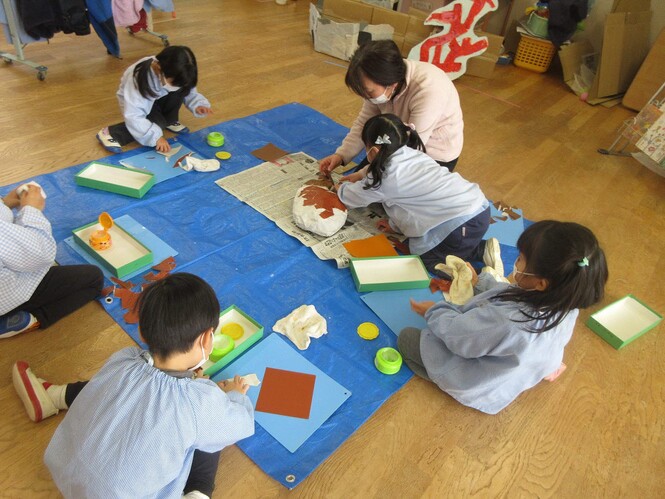 折り紙で、さかなのうろこを作って、立体で作ったさかなにはっている子どもの写真
