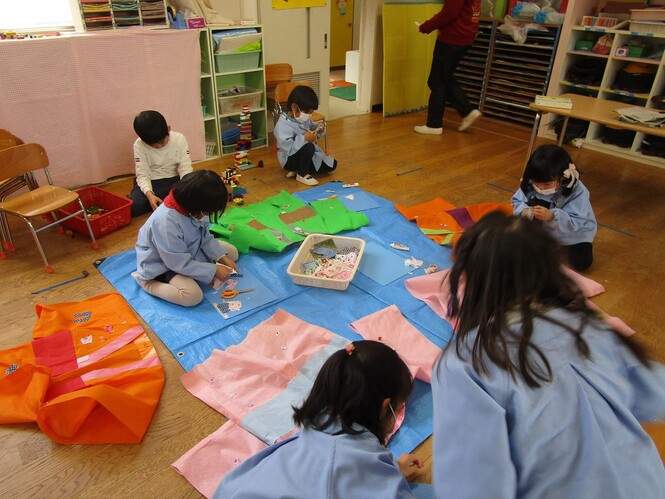 生活発表会で着る不織布で作った着物に飾りをつけている子どもの写真