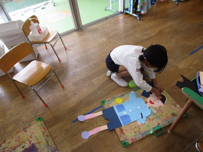画用紙で作った顔や体、足などを糊で貼り合わせている子どもの写真