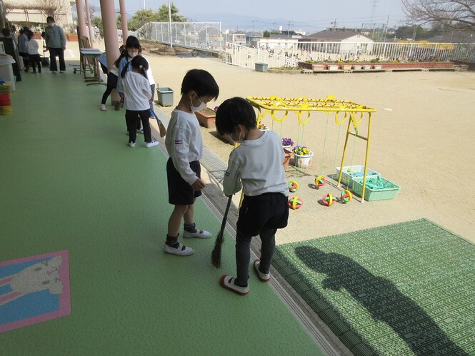 もも組のテラス掃除を見守るすみれ組子どもの写真