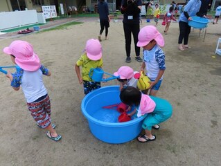 水遊びで使った水で植物に水やりしている子どもたちの写真