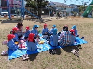 園庭でピクニック弁当をしている子どもたちの写真