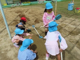 砂場で山を作っている子どもたちの写真